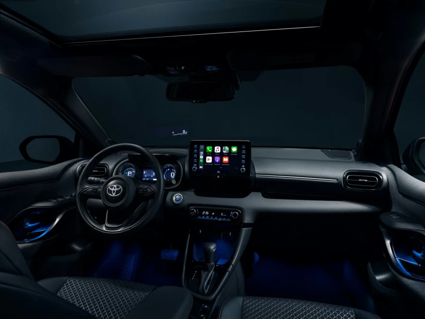 Car interior view showcasing the dashboard, steering wheel, touchscreen display, and modern design elements under dim blue lighting.