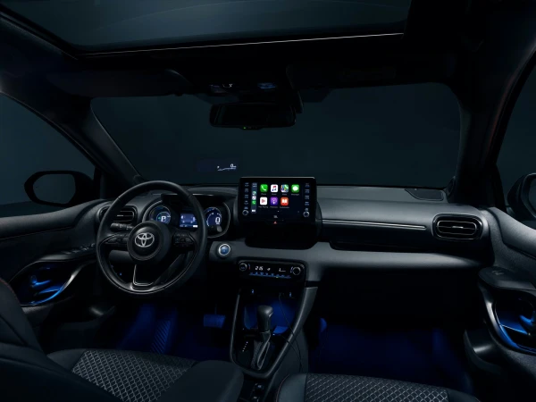 Car interior view showcasing the dashboard, steering wheel, touchscreen display, and modern design elements under dim blue lighting.