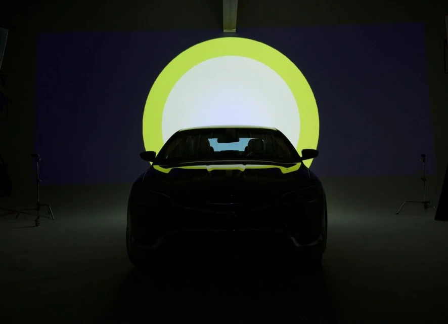 Front view of a dark car in a studio setting, illuminated by a circular light. Dark automobile in shadow against a bright backdrop.