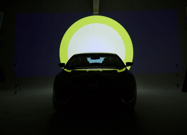 Front view of a dark car in a studio setting, illuminated by a circular light. Dark automobile in shadow against a bright backdrop.