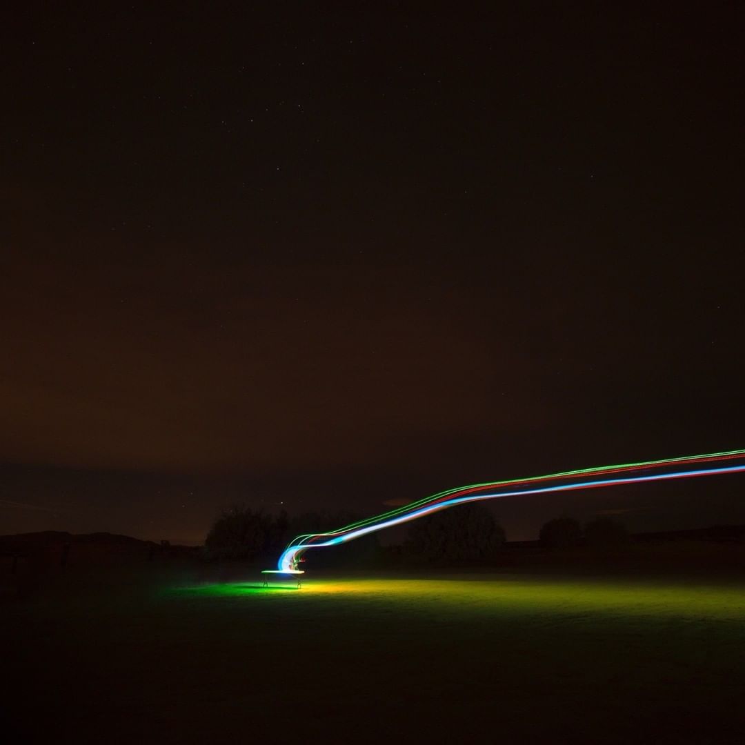 Long exposure photography capturing light trails with green, red, and white hues across a dark night sky with visible stars.