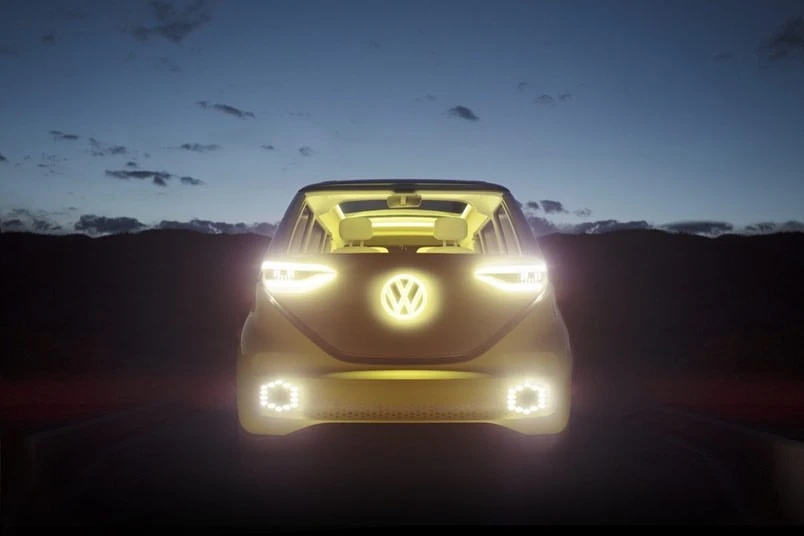 Volkswagen ID Buzz electric van with headlights and logo illuminated at dusk against mountain range and night sky background.
