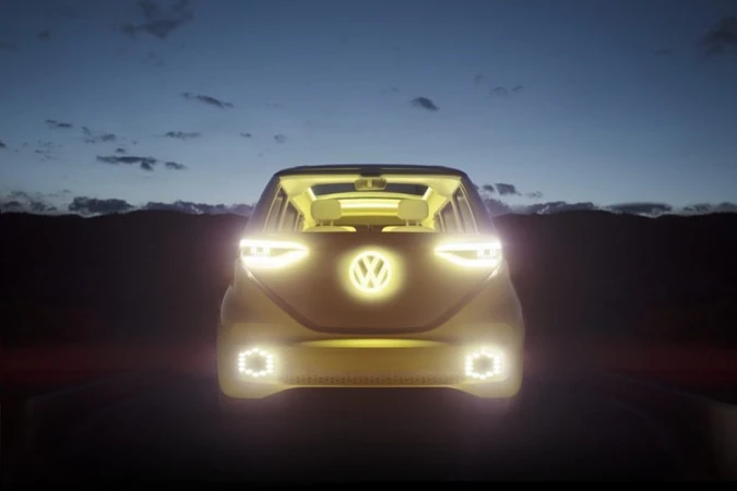 Volkswagen ID Buzz electric van with headlights and logo illuminated at dusk against mountain range and night sky background.