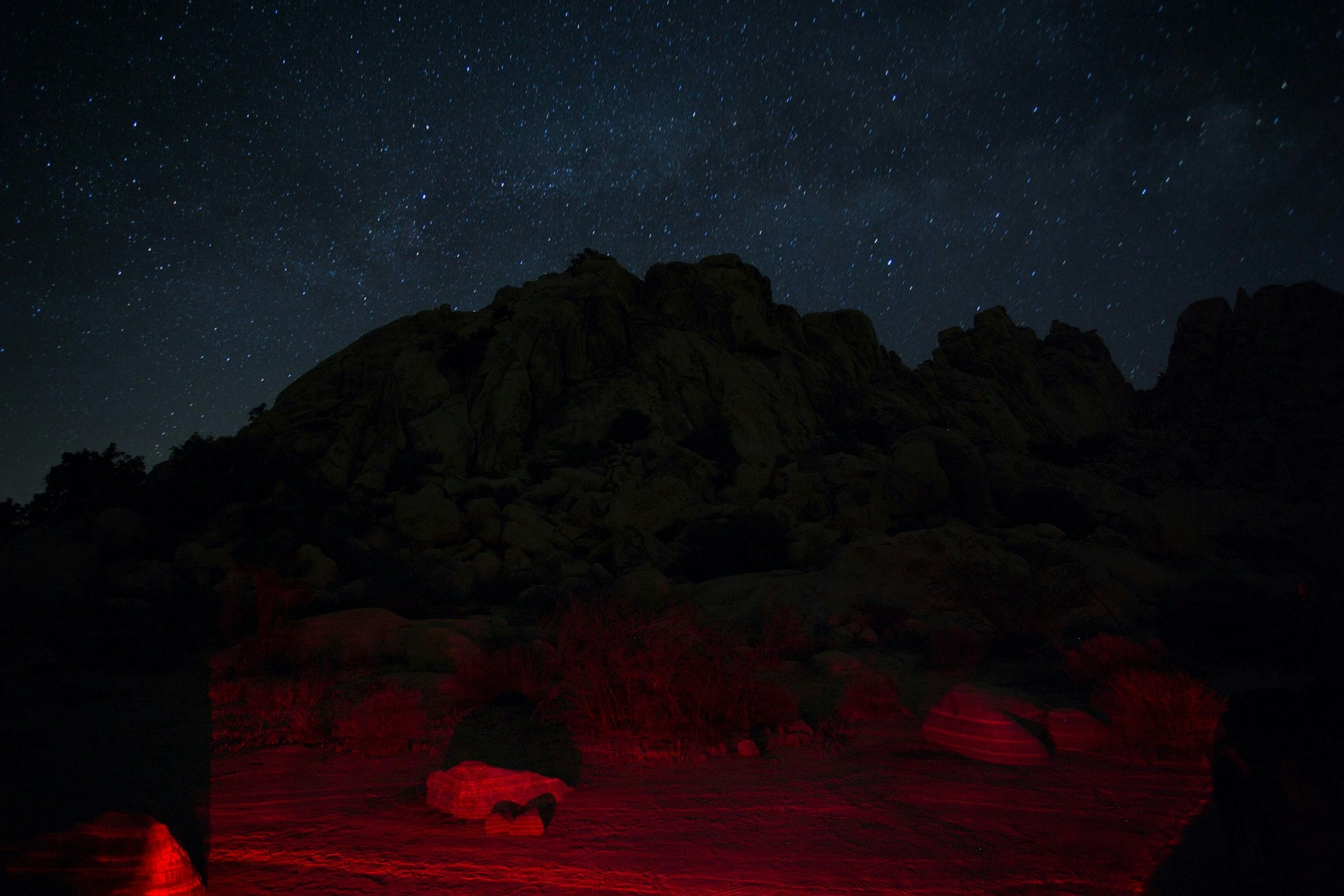 Rocky mountain landscape under a starry night sky with subtle red lighting on the ground by Tobias Hutzler.