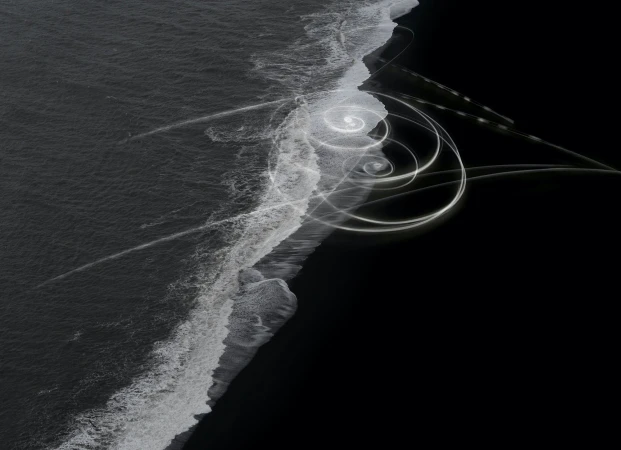 Abstract long exposure of ocean waves washing up on black sand beach with spirals of light painting adding surreal artistic touch.