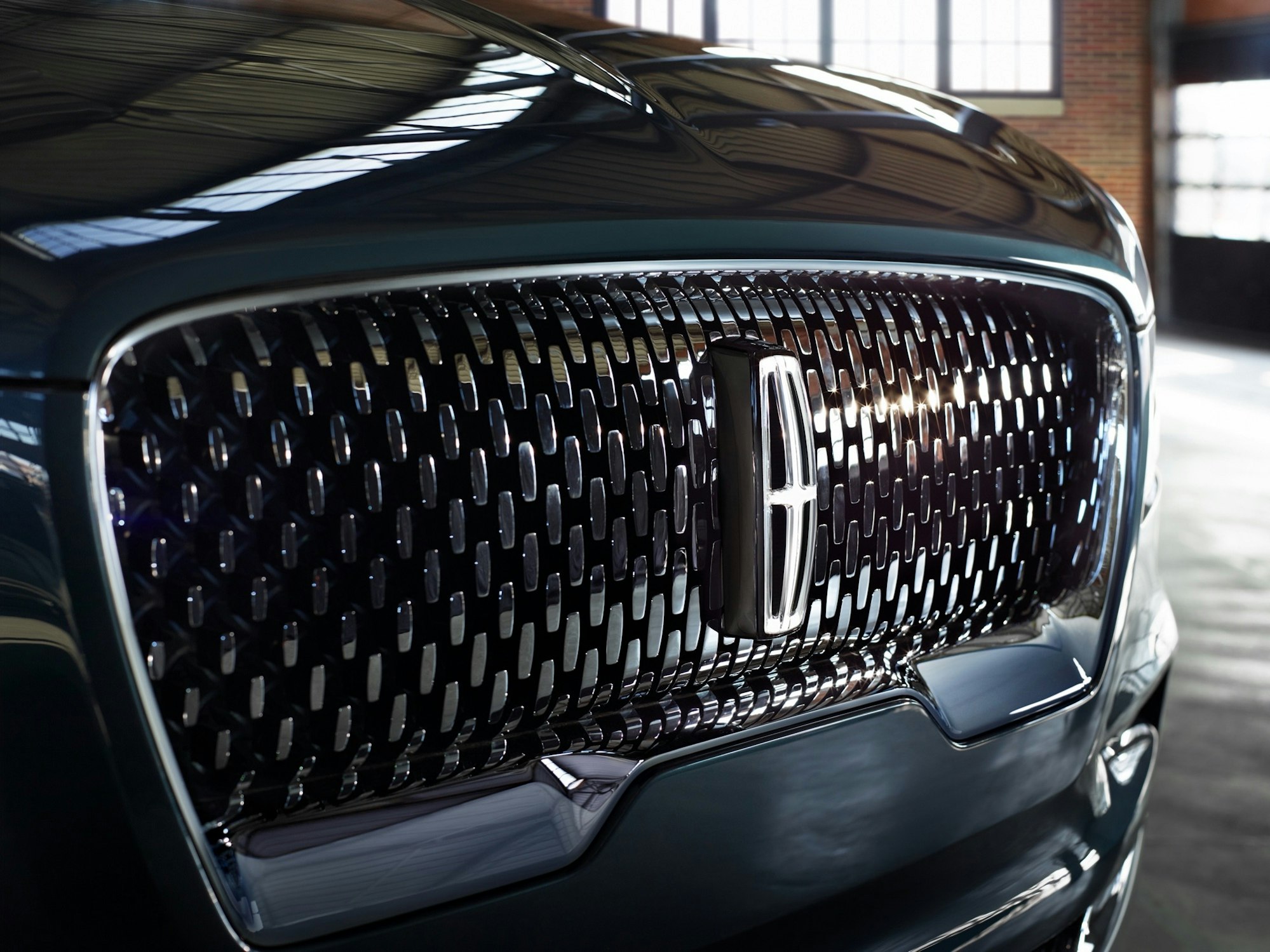 Close-up of a Lincoln car grill with a chrome emblem and a dark green exterior, highlighting the brand's design and luxury.