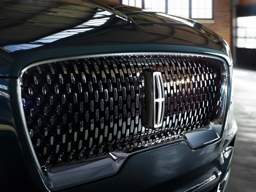 Close-up of a Lincoln car grill with a chrome emblem and a dark green exterior, highlighting the brand's design and luxury.