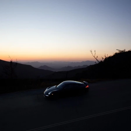 A sleek dark sports car parked on a mountain road at dusk under a gradient twilight sky.