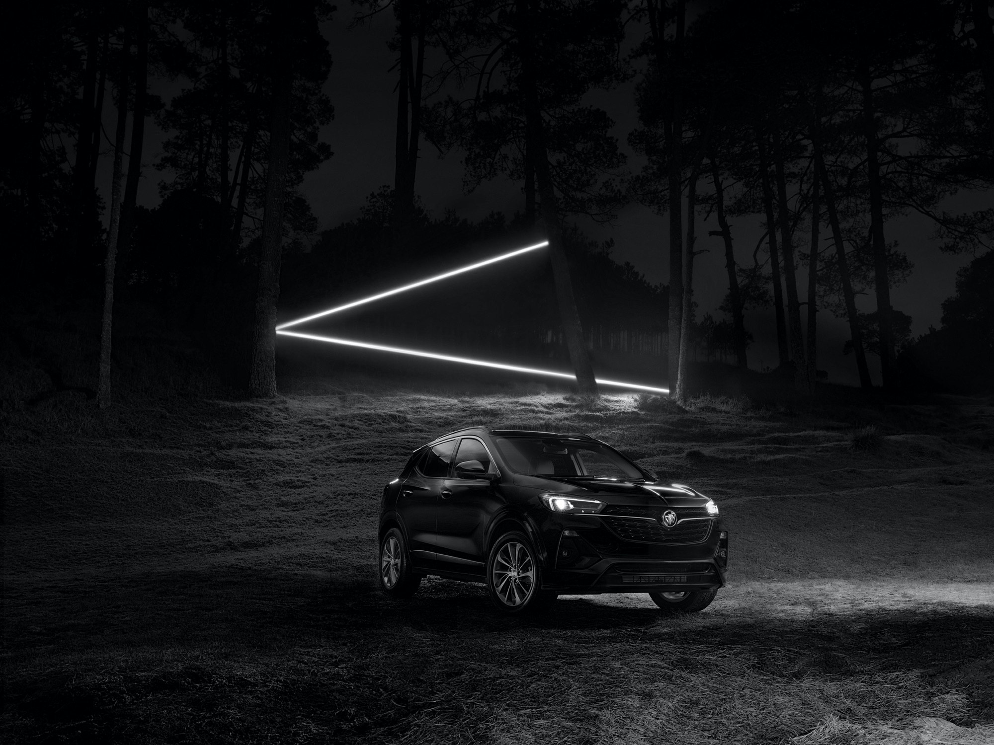 Black Buick Envista SUV parked in a dark forest at night with glowing triangle of neon lights, creating a mysterious automotive image.