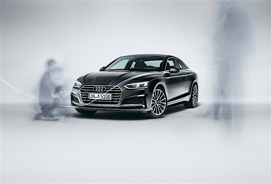 Black Audi coupe parked on a seamless white studio floor with blurred ghostly figures moving around it.