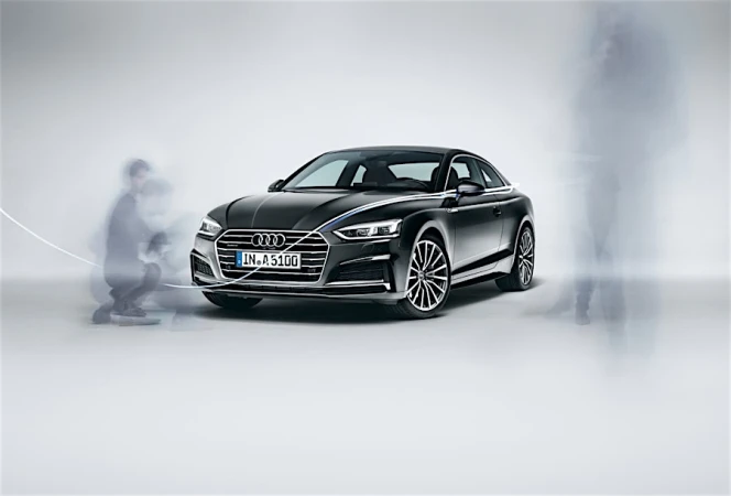 Black Audi coupe parked on a seamless white studio floor with blurred ghostly figures moving around it.