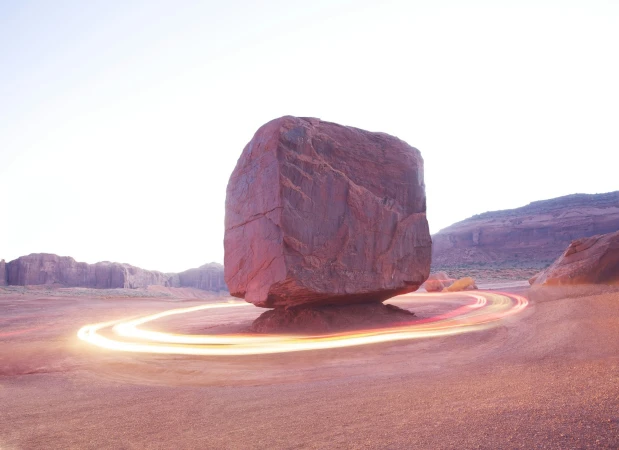 Monument Valley rock formation with light trail around it, creating a surreal desert landscape, illuminated by a bright, natural light.