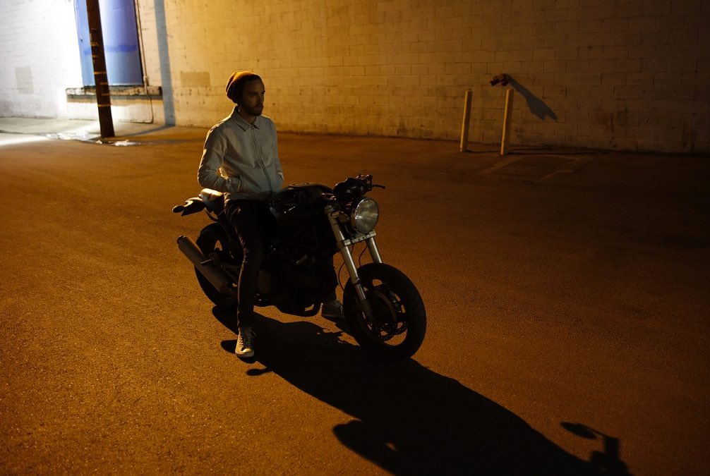 Man seated on a motorcycle parked on an asphalt street at night under warm ambient lighting