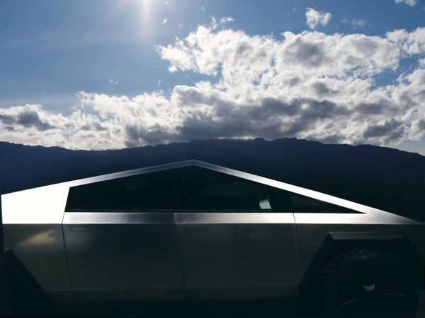 Silver electric pickup truck angled against a mountain backdrop under a dramatic cloudy sky