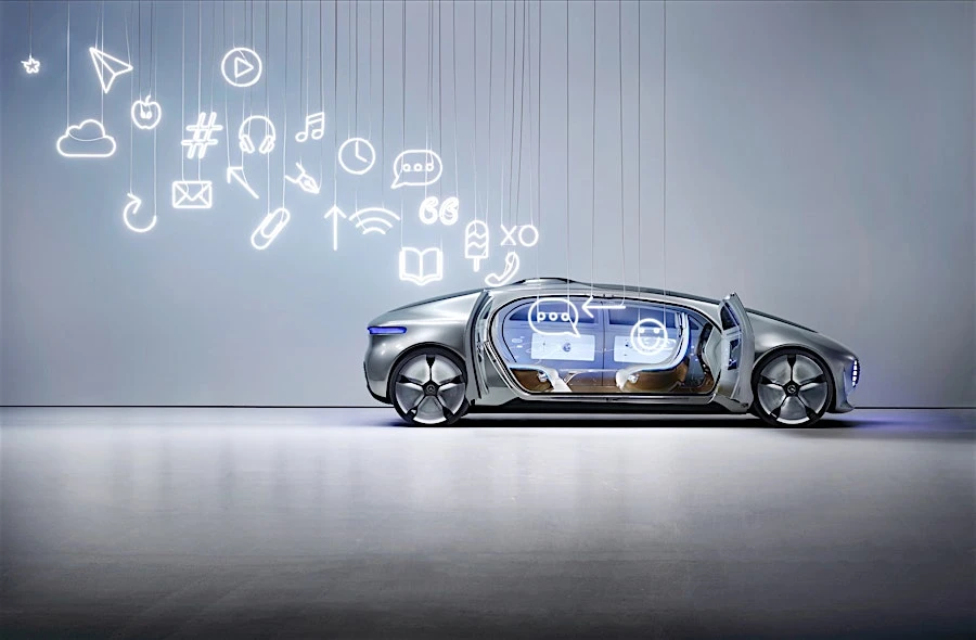 Futuristic silver concept car displayed indoors with illuminated social media icons suspended from the ceiling in a well-lit studio.