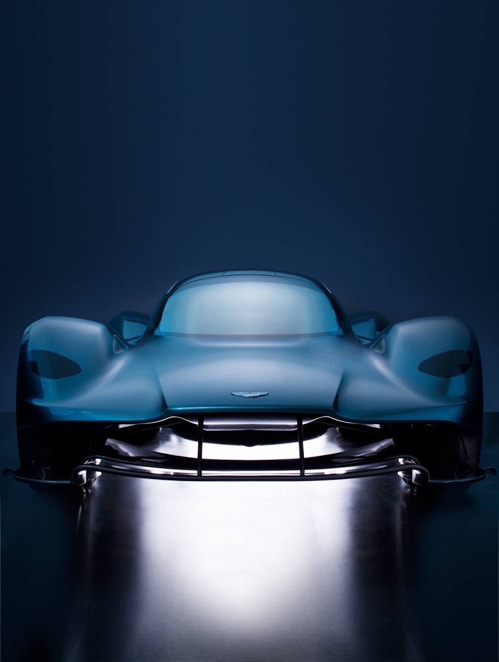 Sleek blue Aston Martin Valhalla supercar showcased in a studio setting, featuring a modern, aerodynamic design under dramatic lighting.