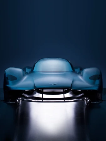 Sleek blue Aston Martin Valhalla supercar showcased in a studio setting, featuring a modern, aerodynamic design under dramatic lighting.