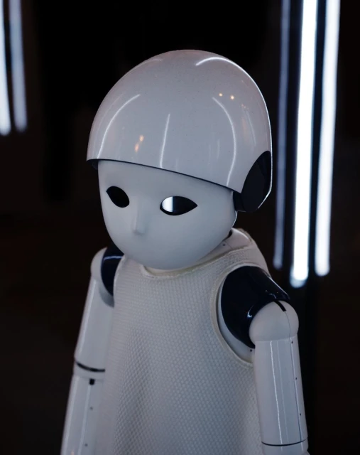Close-up of a white humanoid robot with black accents, featuring a helmet-like head, set against a dark background with vertical lights.