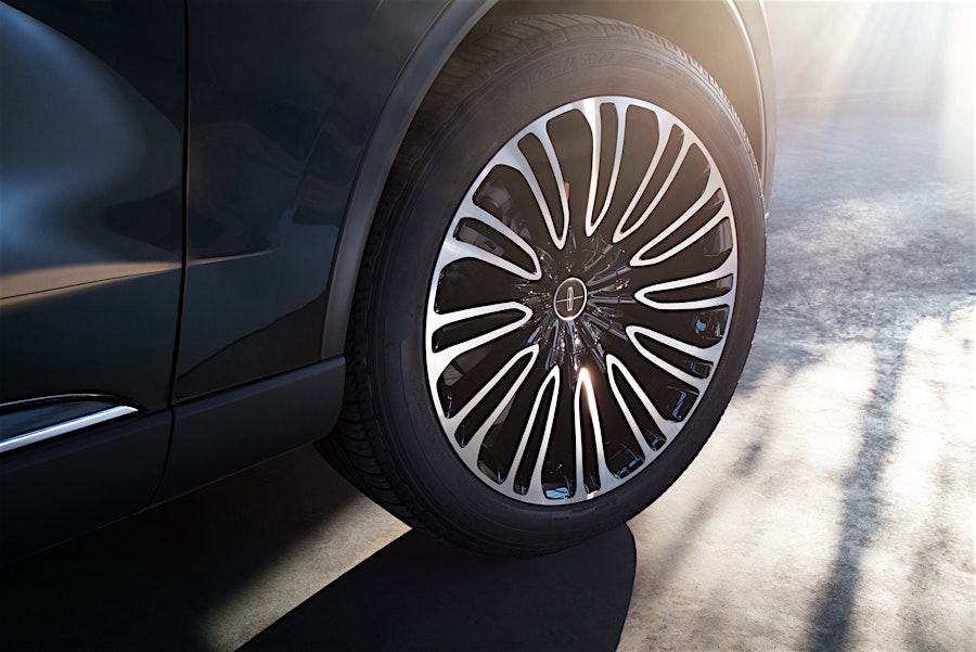 Close-up of a black Lincoln car wheel featuring a detailed silver rim design against a blurred light grey concrete background.