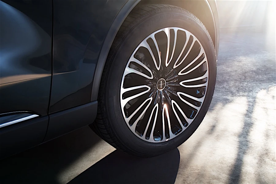 Close-up of a black Lincoln car wheel featuring a detailed silver rim design against a blurred light grey concrete background.