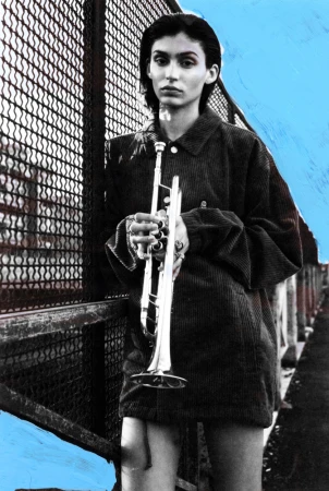 Woman in a dark corduroy jacket holding a silver trumpet against a chainlink fence with bright blue painted background accents.