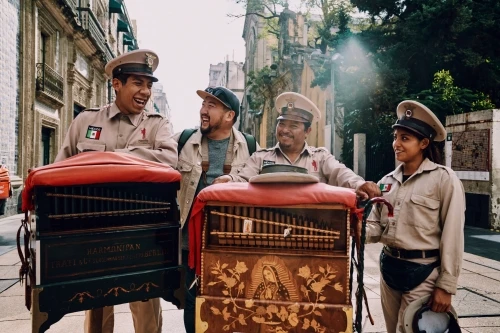 Four street performers with traditional music instruments pose in an urban setting, smiling at the camera on a sunny day.