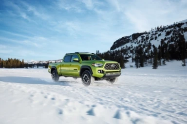Lime green pickup truck driving through a snowy landscape under a bright blue sky with scattered clouds.