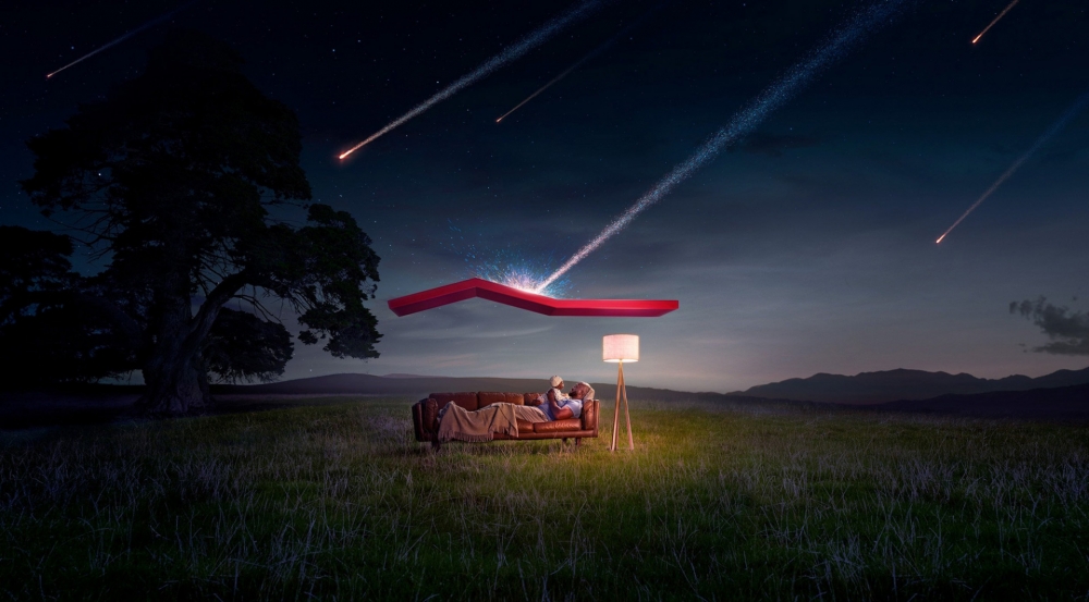 Couple on a couch under a floating red roof in a grassy field at night with meteor showers and mountains in the distance.