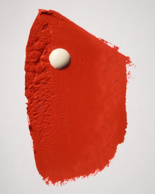 Abstract image: red paint smear on a white background with a white circular object embedded in the red smear.
