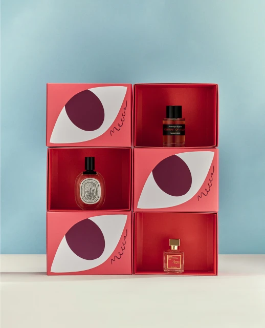 Stacked cubes displaying perfume bottles in a studio setting with geometric eye graphics and a light blue background, product photography.