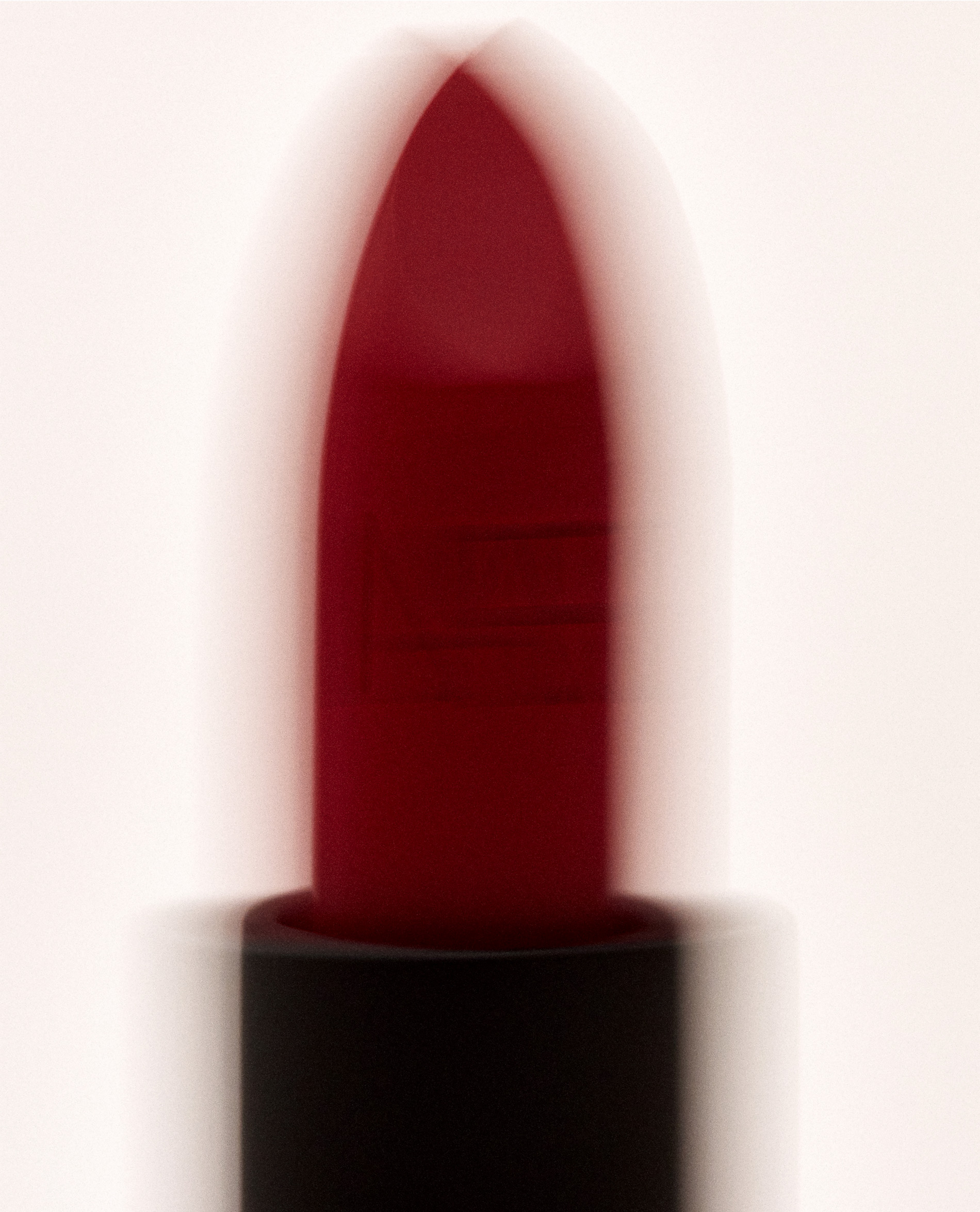 Close-up studio shot of a dark red lipstick tube against a soft white background creating a minimalist and elegant beauty image.