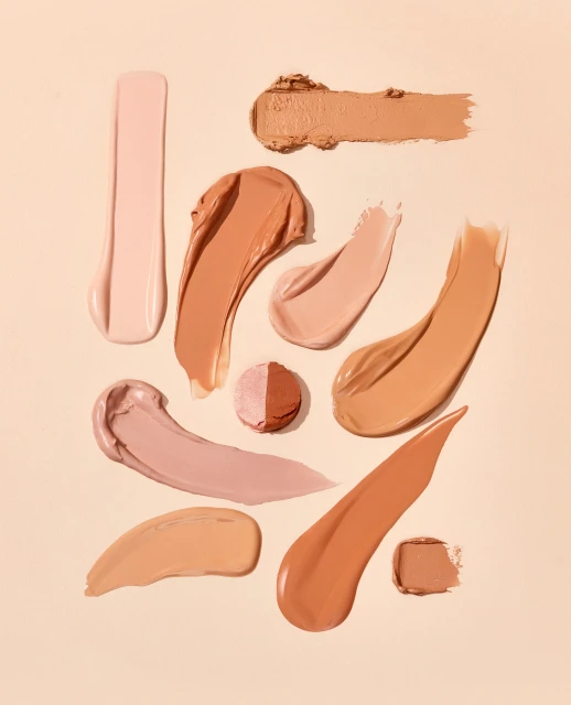 Cosmetics swatches in a variety of skin tone shades are displayed on a beige background, presented in a studio shot for beauty.