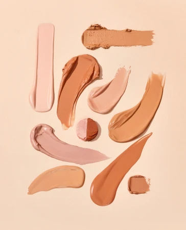 Cosmetics swatches in a variety of skin tone shades are displayed on a beige background, presented in a studio shot for beauty.
