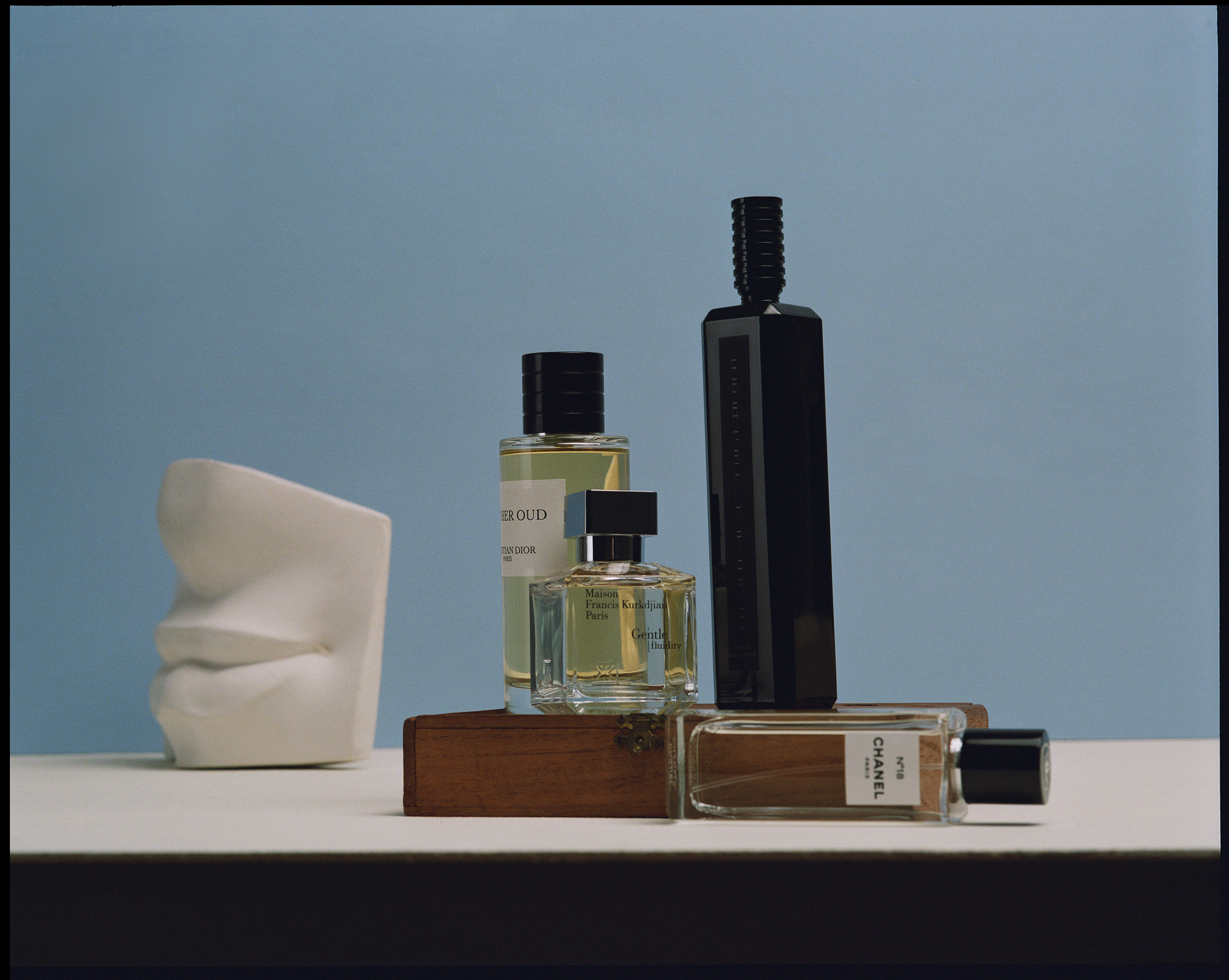 Still life studio shot of an assortment of luxury perfume bottles in various sizes and shapes against a soft blue backdrop.