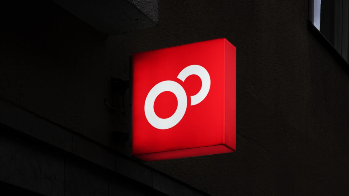 Illuminated red sign with a white graphic logo mounted on the side of a dark building during the night, creating a stark contrast.