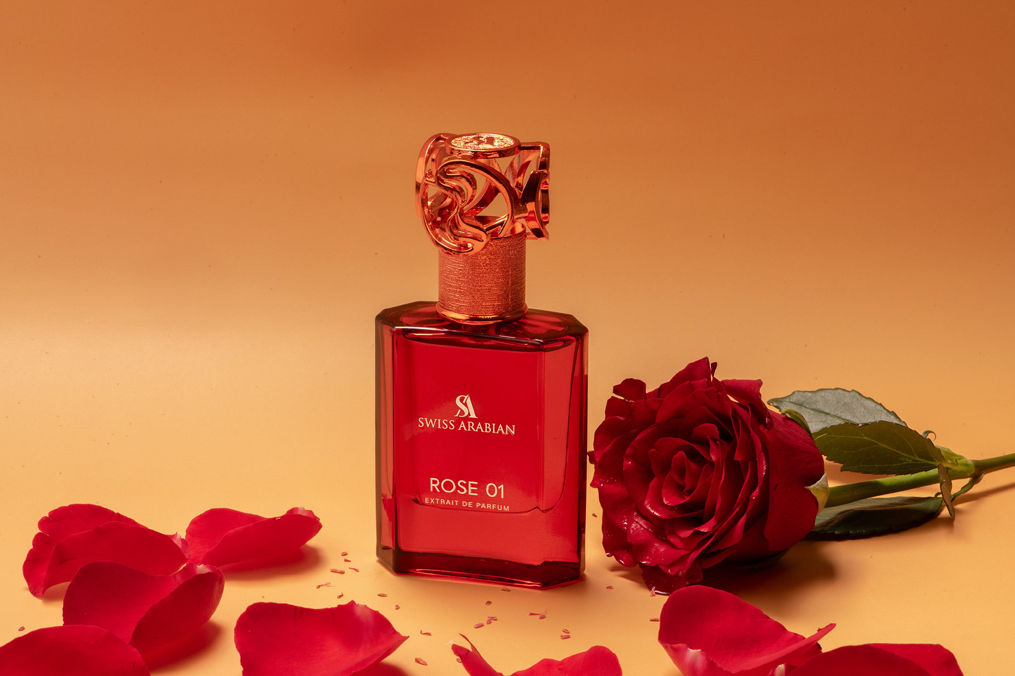 Close-up studio shot of red Swiss Arabian Rose 01 perfume bottle with decorative cap, a single rose, and loose petals.