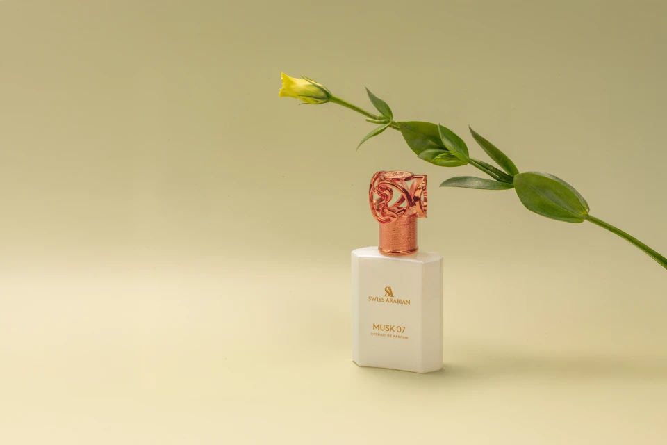 Elegant perfume bottle with copper accents, paired with a delicate yellow flower and green leaves, against a soft light yellow background.