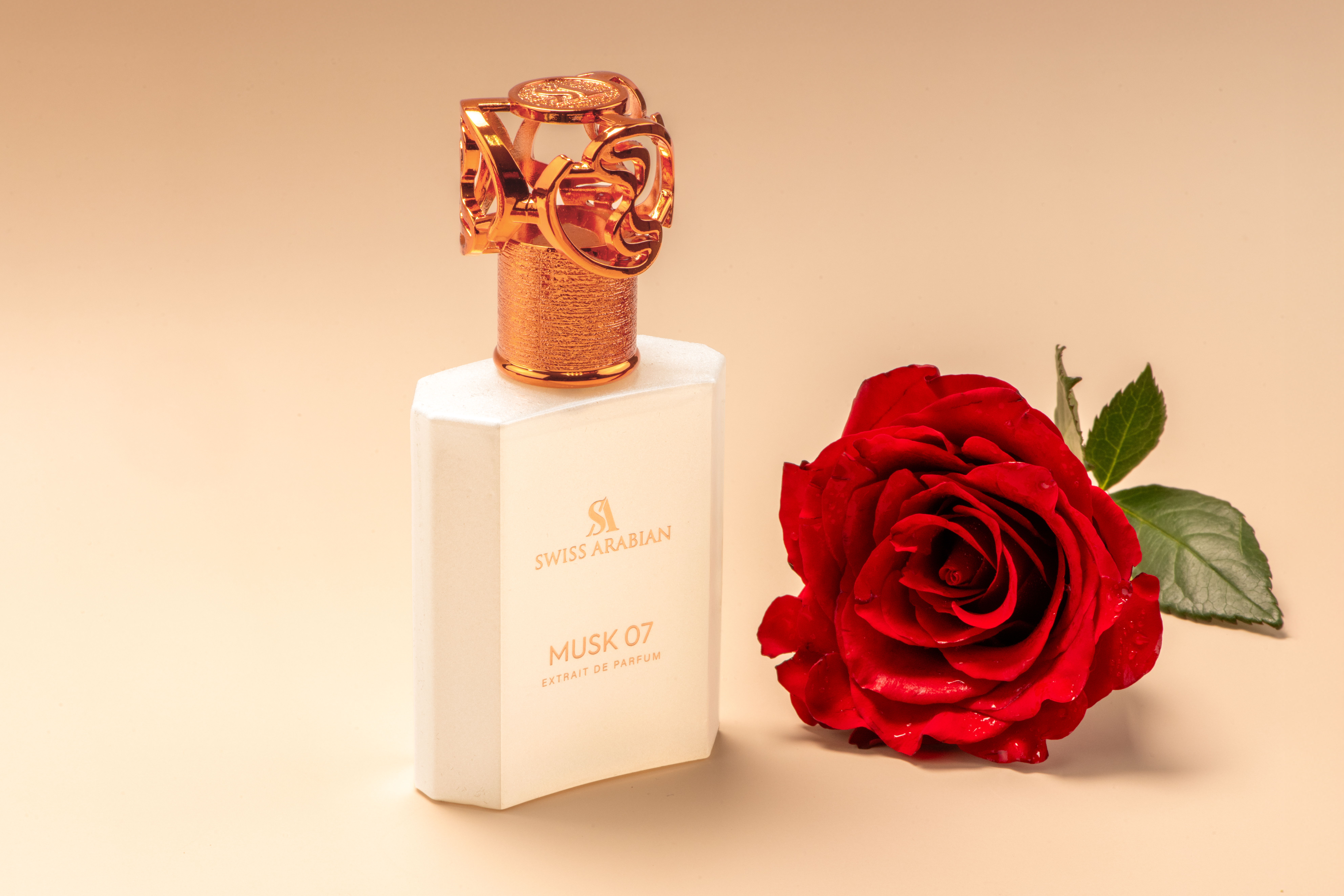 Elegant presentation of Swiss Arabian Musk 07 perfume with intricate gold cap, paired with a vibrant red rose on a neutral surface.