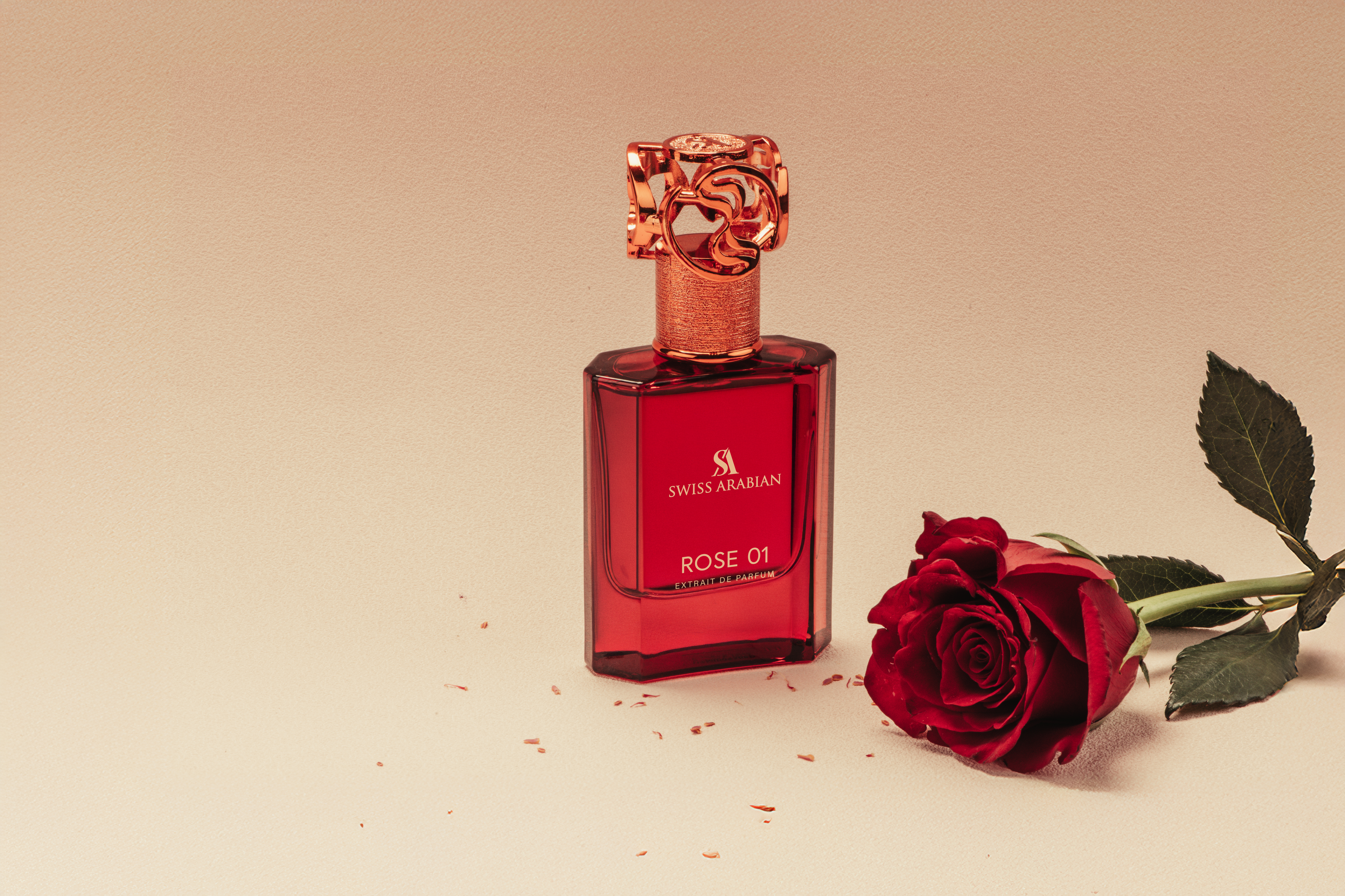 A red-toned still life featuring a 'Swiss Arabian' perfume bottle and a red rose on a cream-colored surface. Focus on beauty and fragrance.