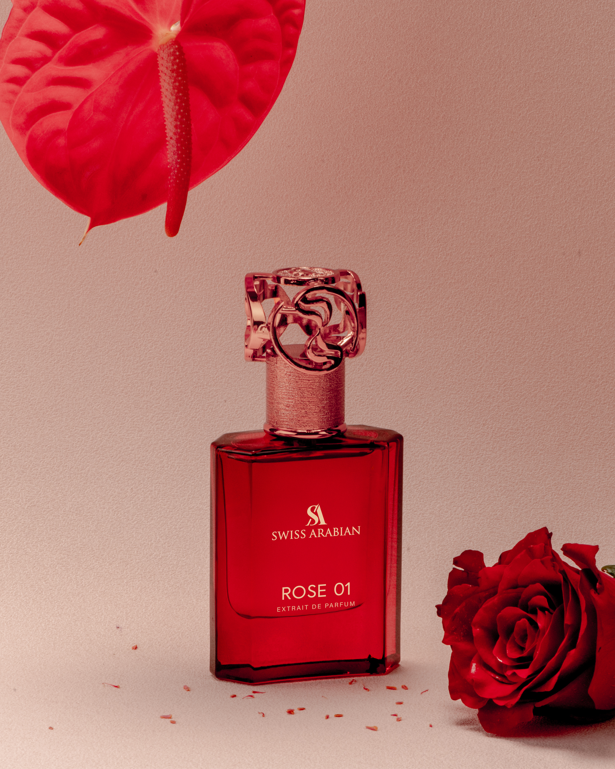 Elegant product shot of a red glass Swiss Arabian perfume bottle with a decorative cap, accented by a red anthurium and rose.