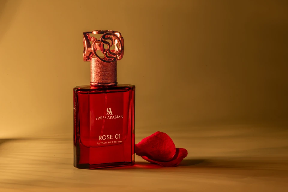Elegant red perfume bottle with gold accents and a rose petal on a gold surface in a studio with diffused lighting.