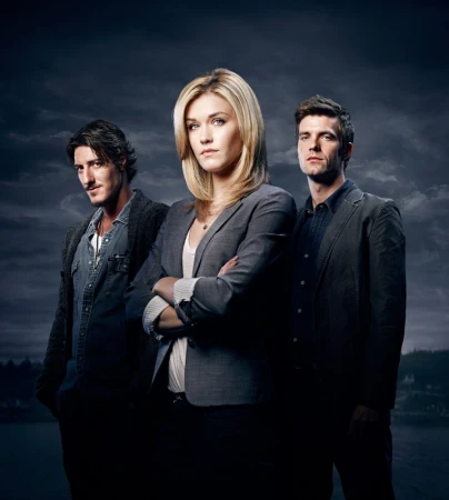 Studio portrait of three actors in blazers and a denim jacket against a cloudy dark blue sky with water and land visible in the distance.