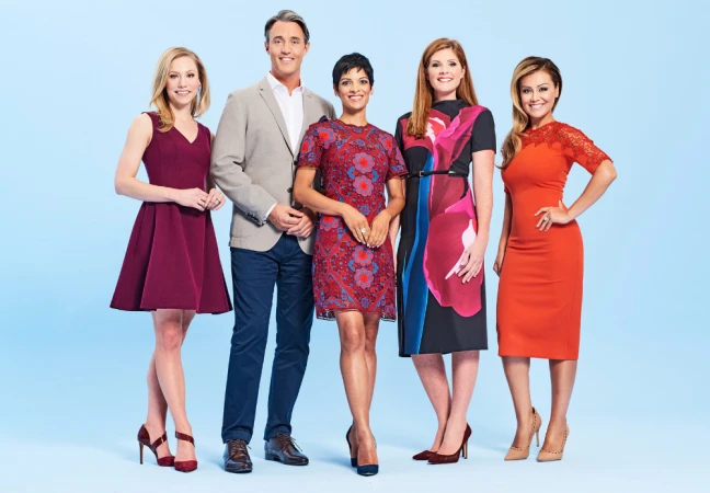 Group portrait of five news presenters in dresses and a jacket, standing in a row against a studio backdrop with a light blue gradient.