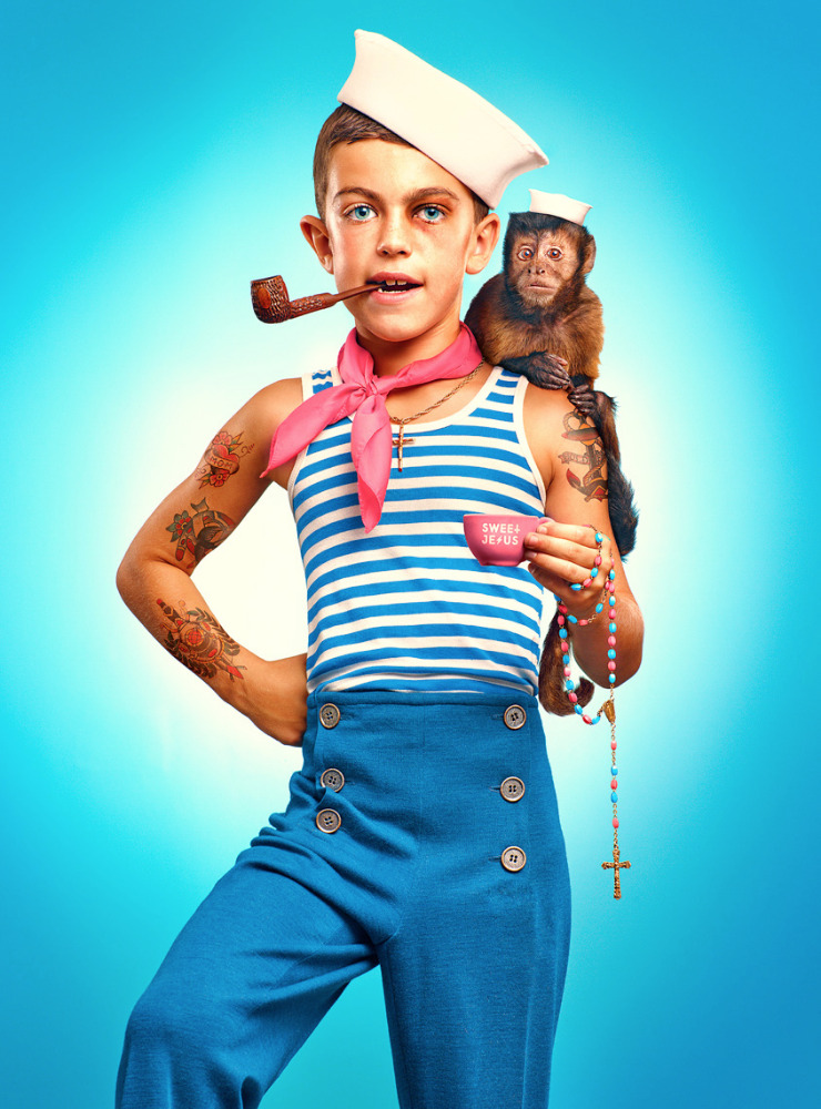 Young boy in a sailor outfit with tattoos and a pipe, accompanied by a monkey, posing against a light blue gradient background.