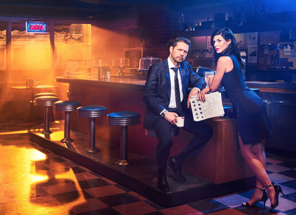 A stylish photo of a man in a suit and a woman in a dress sitting at a diner counter with a classic American aesthetic and warm lighting.