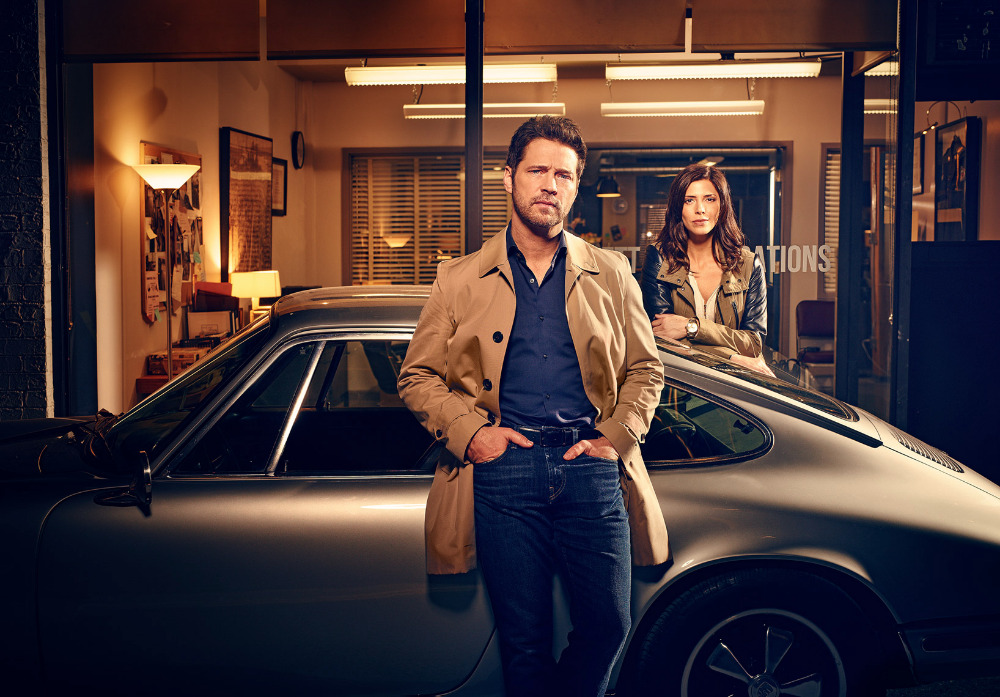 Man and woman standing beside a vintage silver sports car outside an office building at twilight by photographer Matt Barnes.