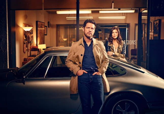Man and woman standing beside a vintage silver sports car outside an office building at twilight by photographer Matt Barnes.