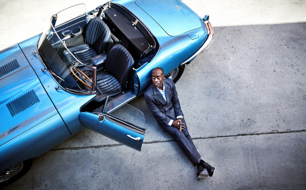 An African-American man in a suit leans against a light blue classic convertible car, adding a touch of luxury and elegance to the scene.