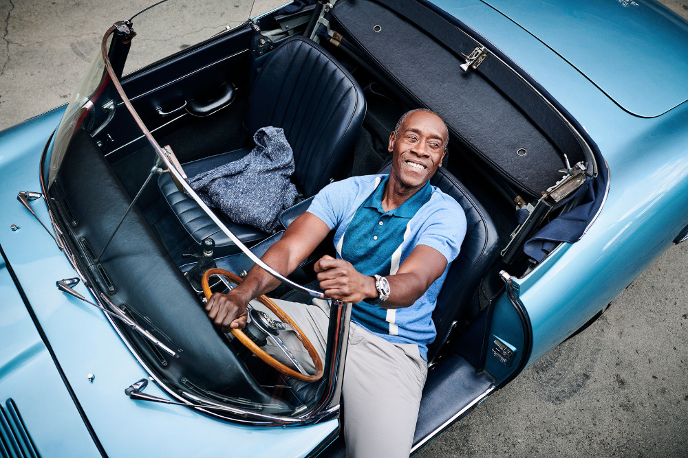 Adult male driving a light blue convertible car with a wooden steering wheel. The man smiles broadly while holding the wheel.