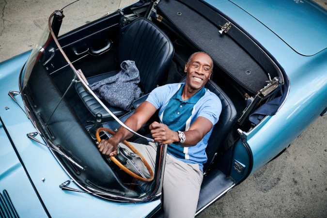 Adult male driving a light blue convertible car with a wooden steering wheel. The man smiles broadly while holding the wheel.